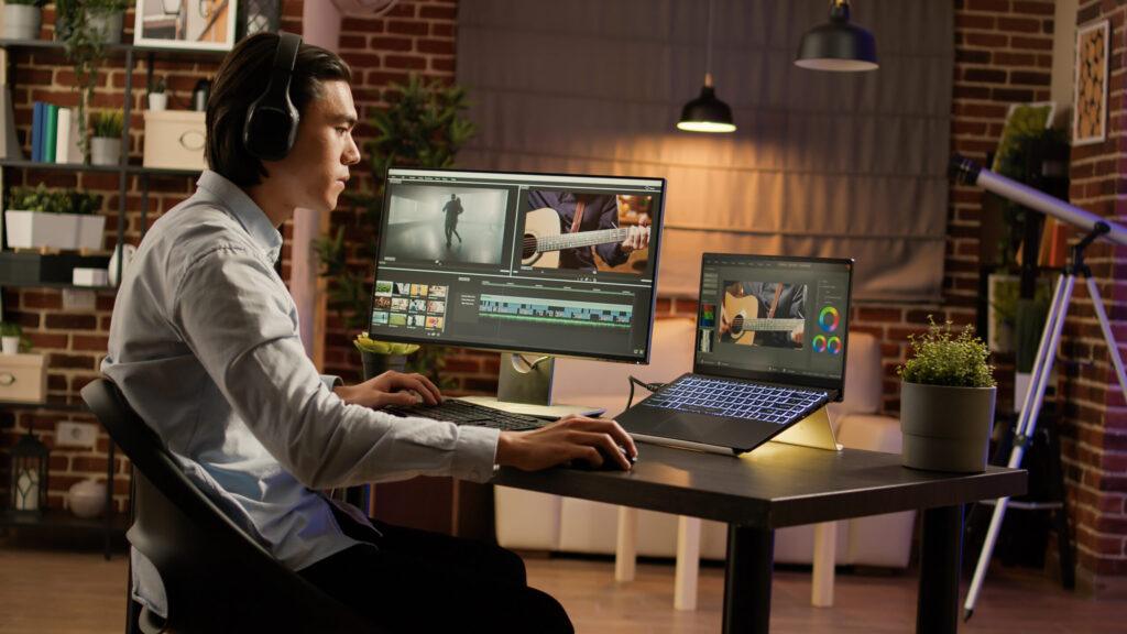 A man seated at a desk, working on two computer monitors displaying various applications.