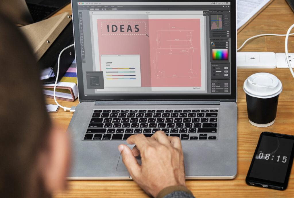 Individual using a laptop adorned with a unique design, engaged in work at a desk with natural light.