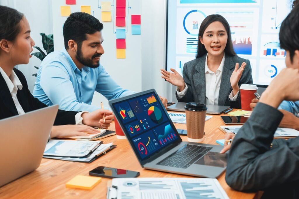 A group of business professionals seated at a table, each using laptops for a collaborative meeting.